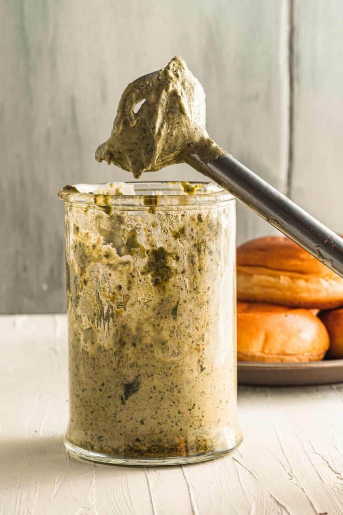 Pesto mayo in container with immersion blender on top of it.