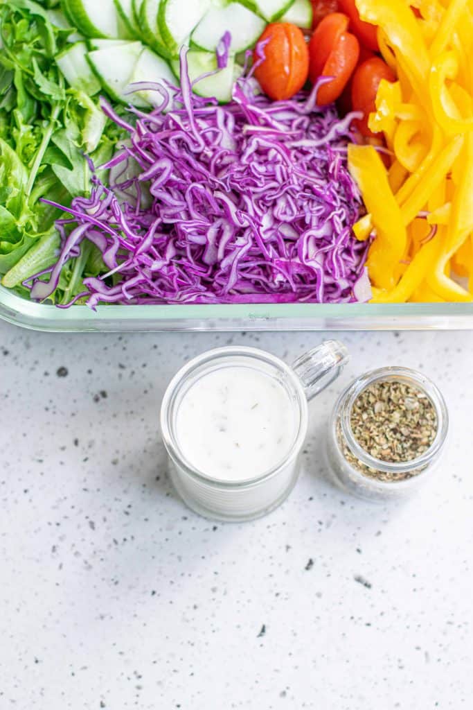 Overhead photo of purple cabbage, yellow bell pepper and greens in a glass dish with Greek yogurt and fresh herbs beside it.