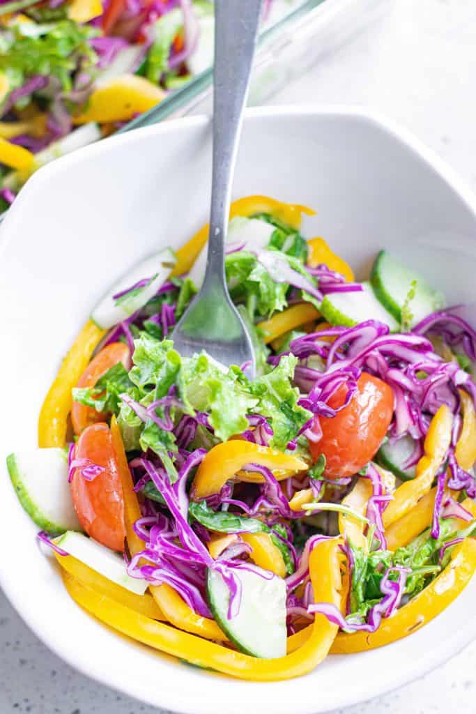 Rainbow salad in a white bowl with a fork in it.