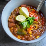 Bowl of vegan chili topped with lime slices and cilantro.