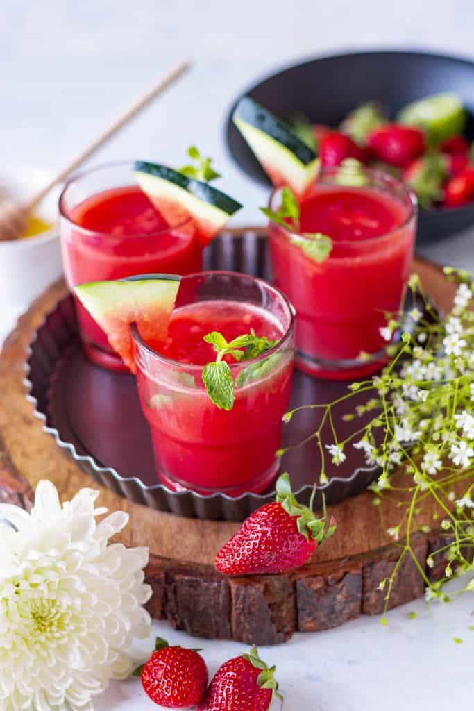 Three glasses of Watermelon Strawberry Limeade on a wooden platter.