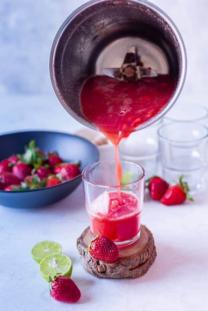 Pouring watermelon strawberry limeade out of blender and a glass.