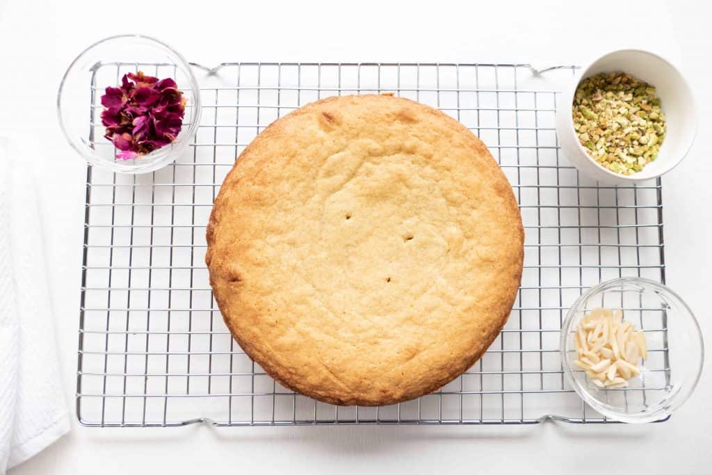 Cake on a wire cooling rack with garnishes beside it.