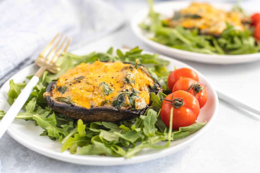 Side view of cheesy mushrooms on greens with cherry tomatoes on the side.