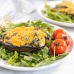 Side view of cheesy mushrooms on greens with cherry tomatoes on the side.