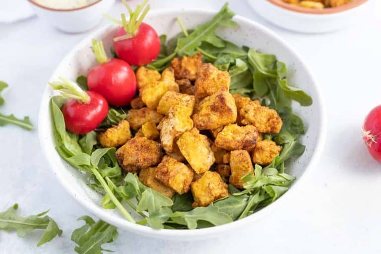 Air Fryer Tofu Nuggets on a bed of greens with three radishes on the side.