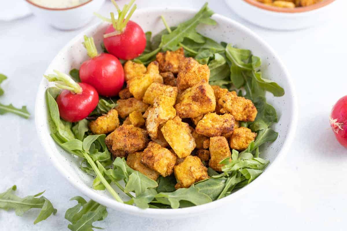 Air Fryer Tofu Nuggets on a bed of greens with three radishes on the side.