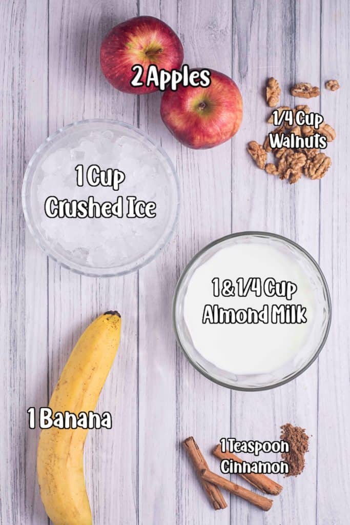 Apples, banana, walnuts, ice, cinnamon and almond milk on a white board.