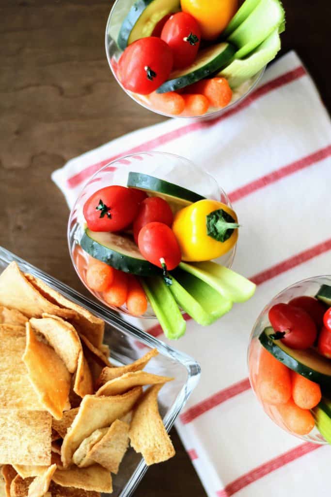 Overhead view of vegetables and dip in cups with bowl of crackers on the side.