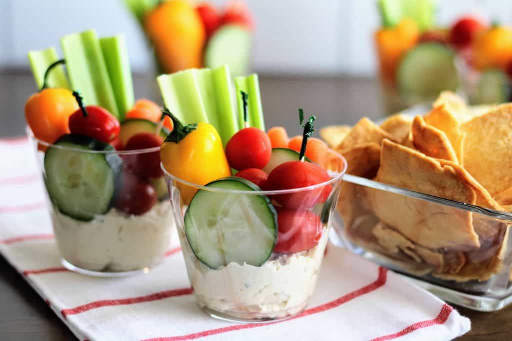 2 cups with veggies and hummus on a dish towel with cracks beside it.