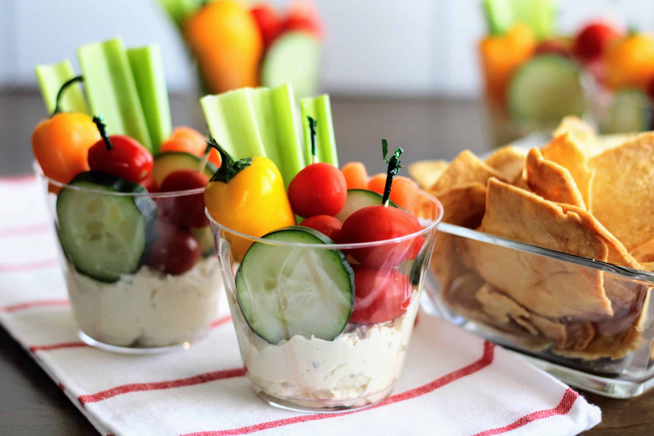 2 cups with veggies and hummus on a dish towel with cracks beside it.