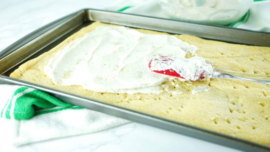 Cream cheese spread on dough on a baking sheet.