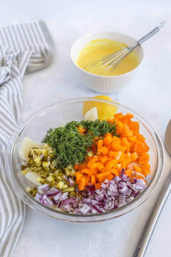 Dill potato salad ingredients in a bowl with dressing behind it.