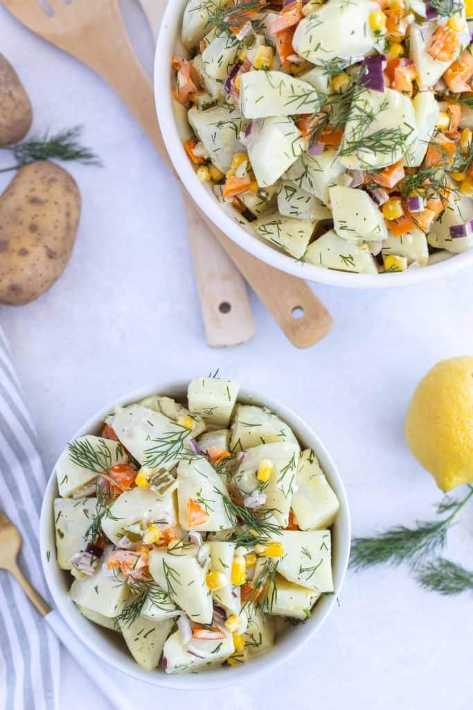 Dill potato salad in a serving bowl with a smaller white bowl of potato salad diagonal from it.