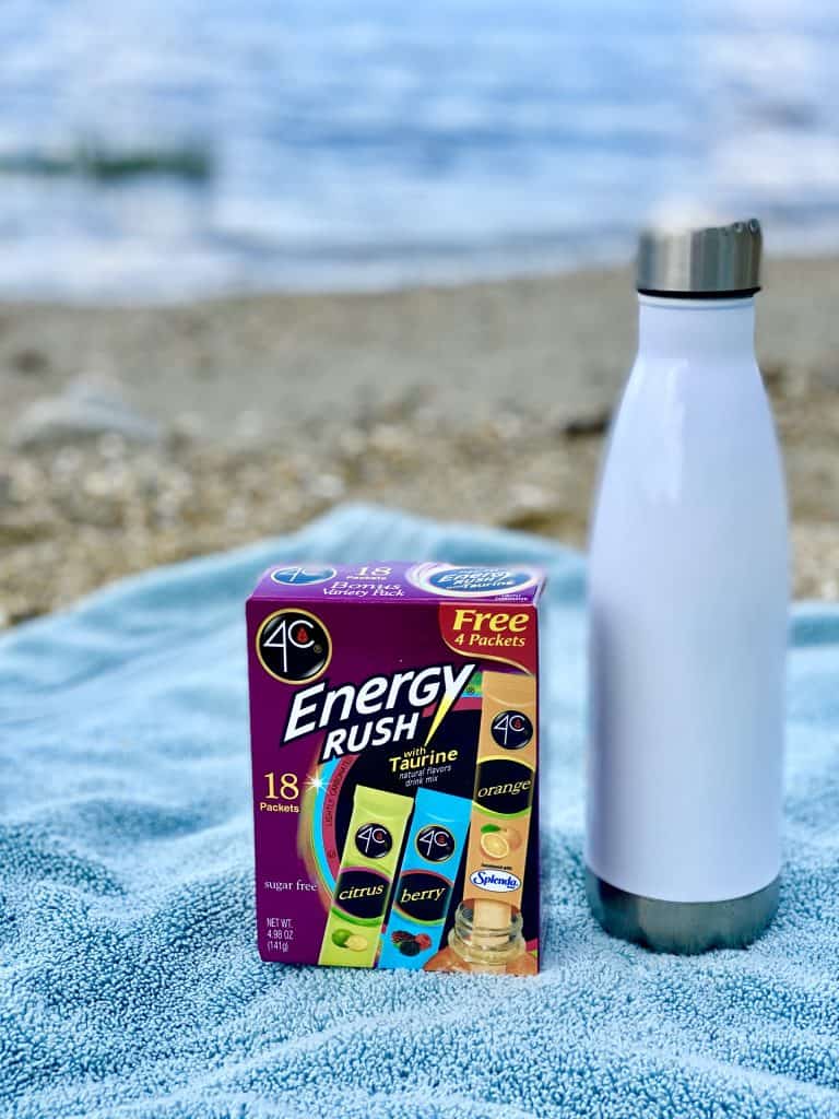 Energy Rush packets with water bottle on beach towel with ocean in the background.