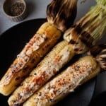 Grilled corn with the husks pulled back on a black [late.