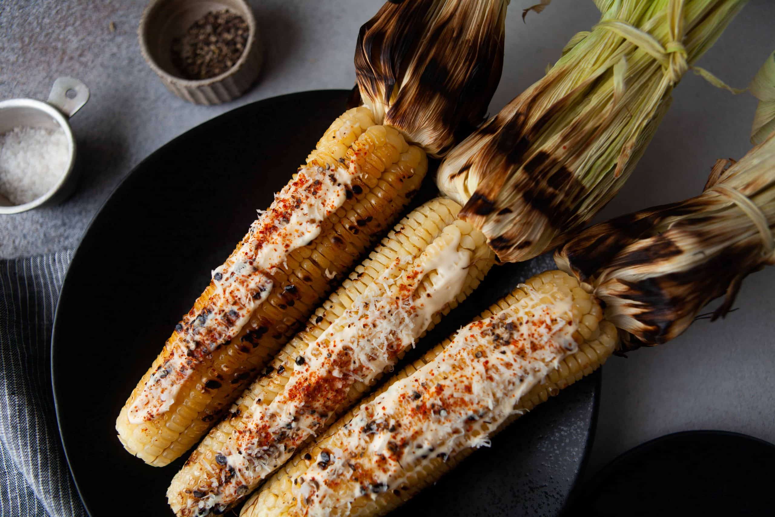 Grilled corn with the husks pulled back on a black [late.