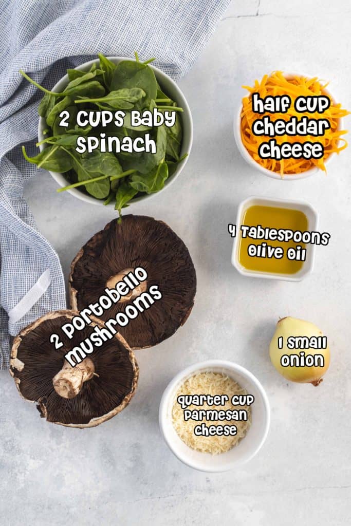 Spinach, cheddar cheese, portobello mushrooms, olive oil, onion and Parmesan cheese on a white counter..