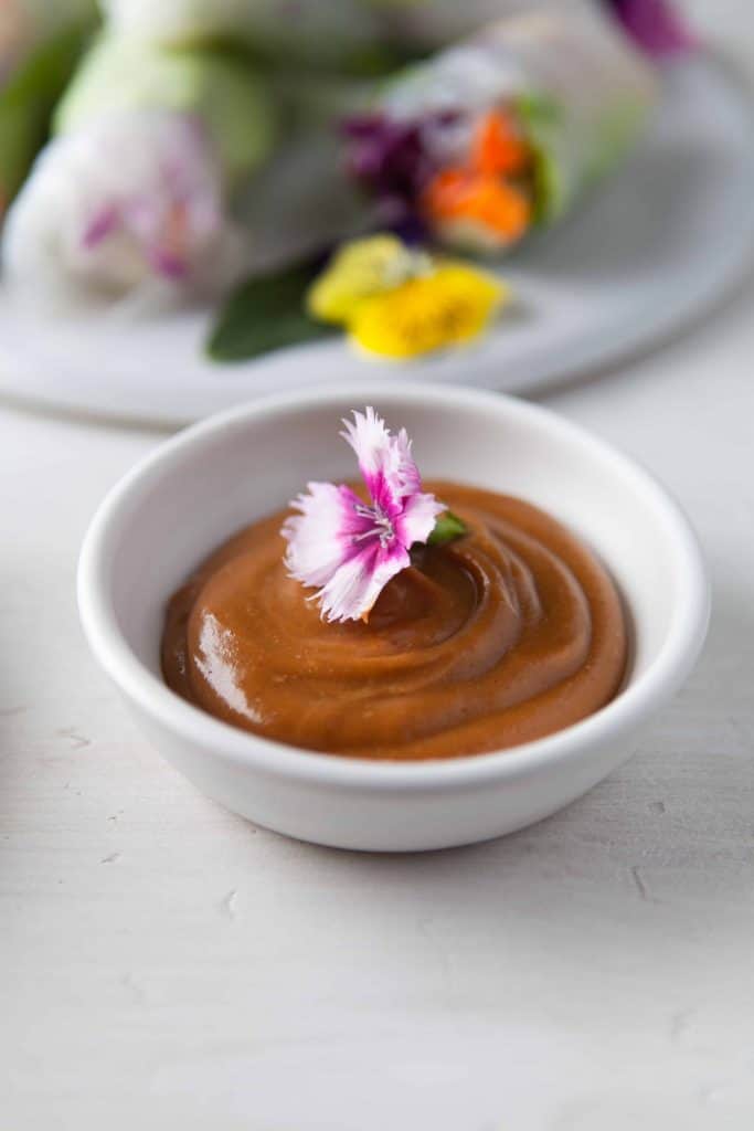 Small bowl of peanut sauce with edible flower on top.