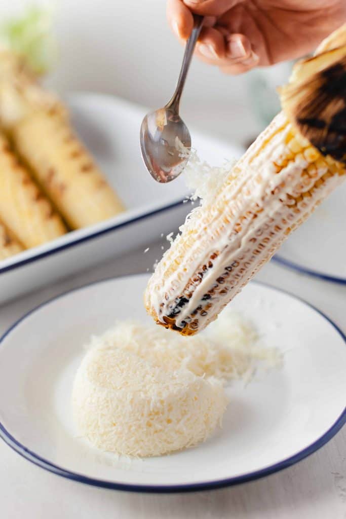 Sprinkling cheese on grilled corn on the cob.