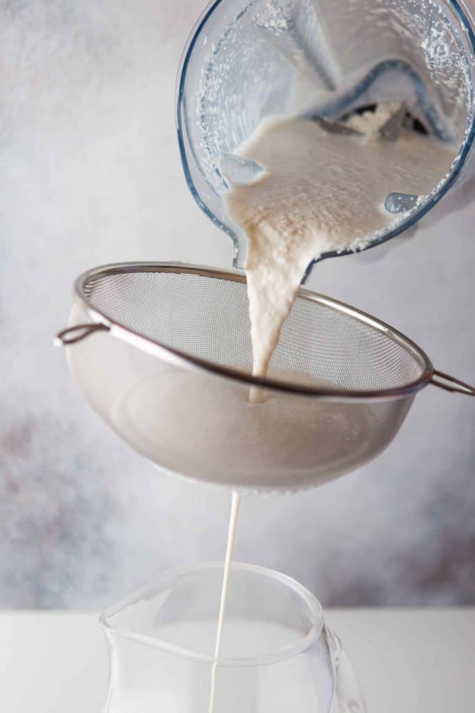 Straining coconut punch over a bowl.