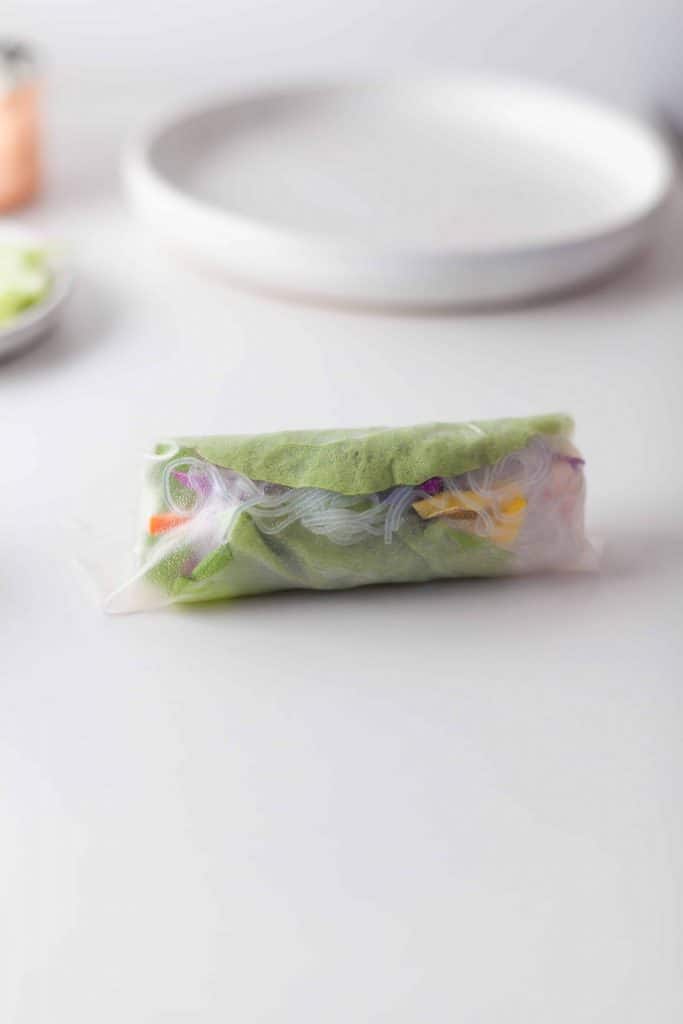 Single spring roll wrapped without garnishes on a white background.