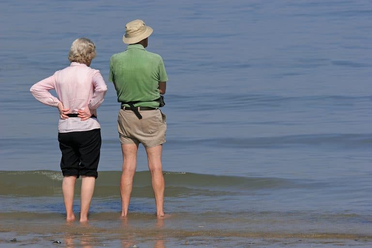 Elderly man and woman standing together and paddling at the beach.