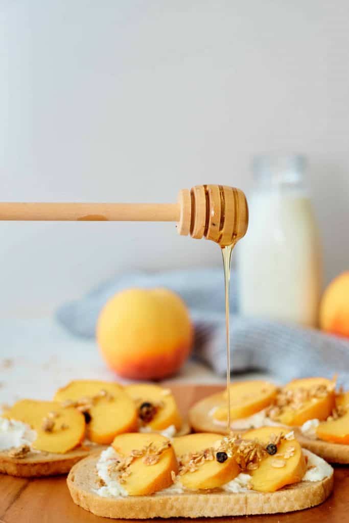 Honey being drizzled on top of peach toast.