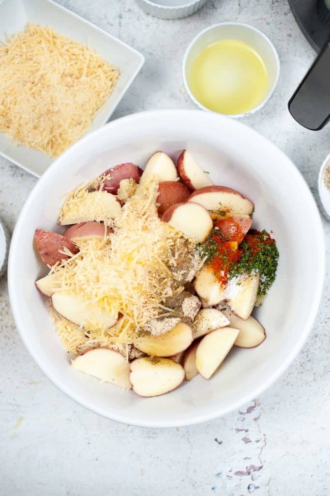 Potatoes, cheese and herbs in a white bowl.