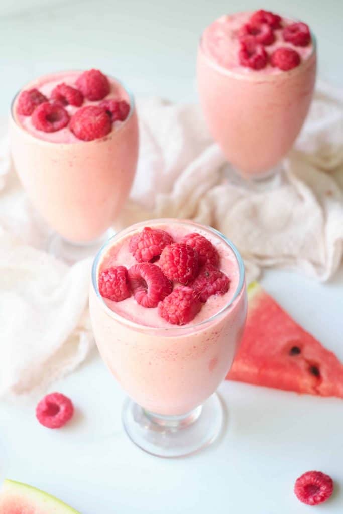 Three raspberry watermelon milkshakes topped with fresh raspberries.