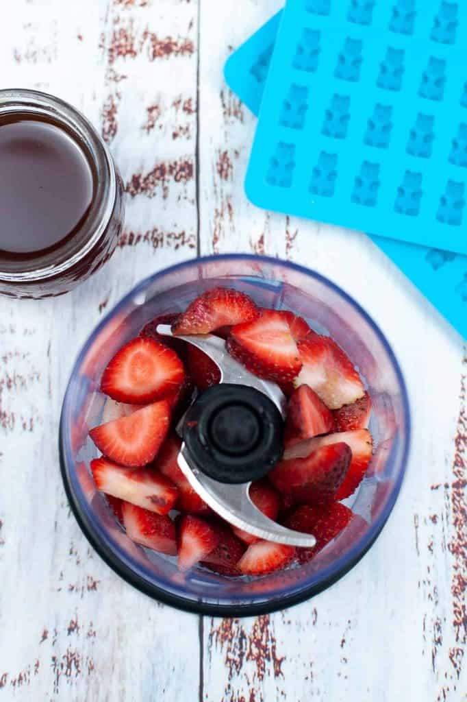 Blending strawberries in a blender with gummy bear mold on the side.