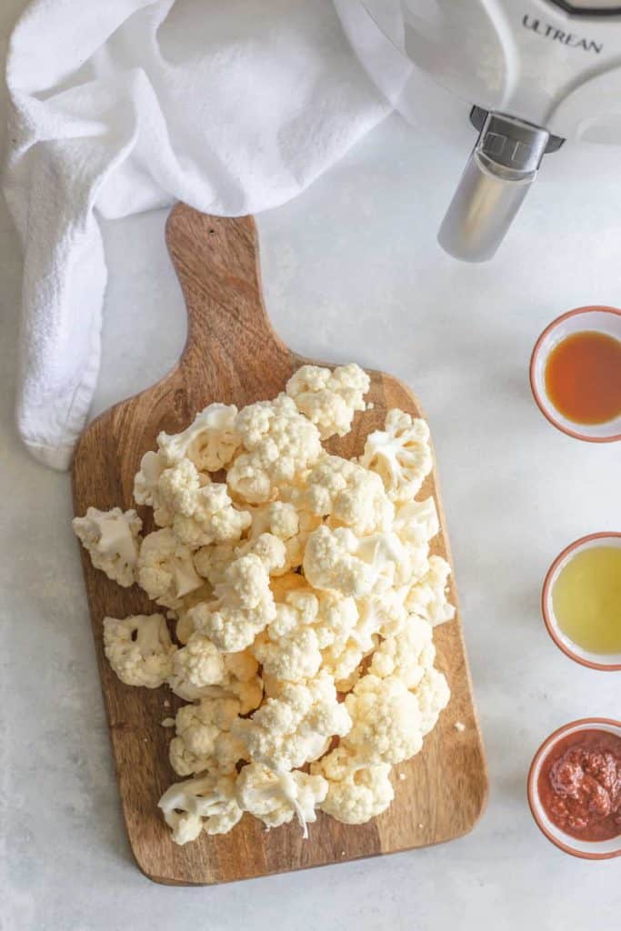 Cauliflower cut up on a cutting board with spices beside iit.