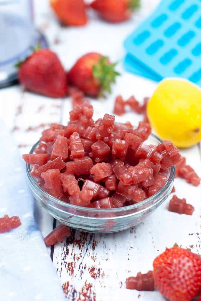 Dish of gummy bears with fresh strawberries and lemon behind it.