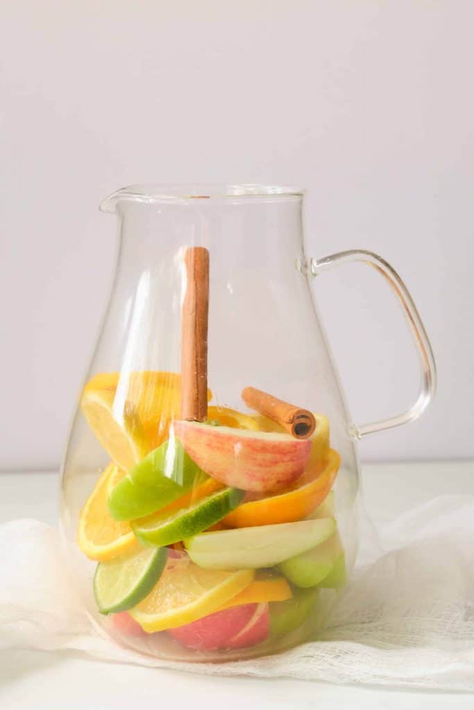 Fruit in a glass pitcher with a cinnamon stick in the center.