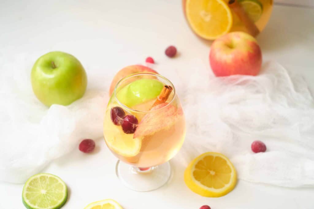Glass of white sangria with fruit surrounding it.