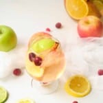 Glass of white sangria with fruit surrounding it.