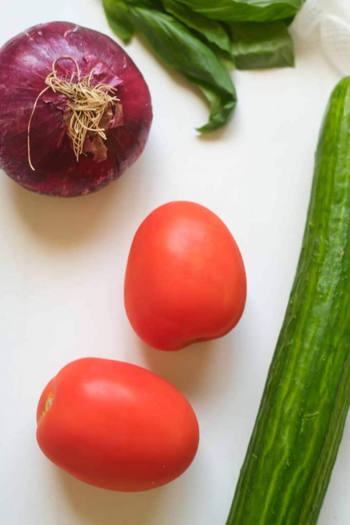red onion, basil, cucumber, and Roma tomatos on a white background.