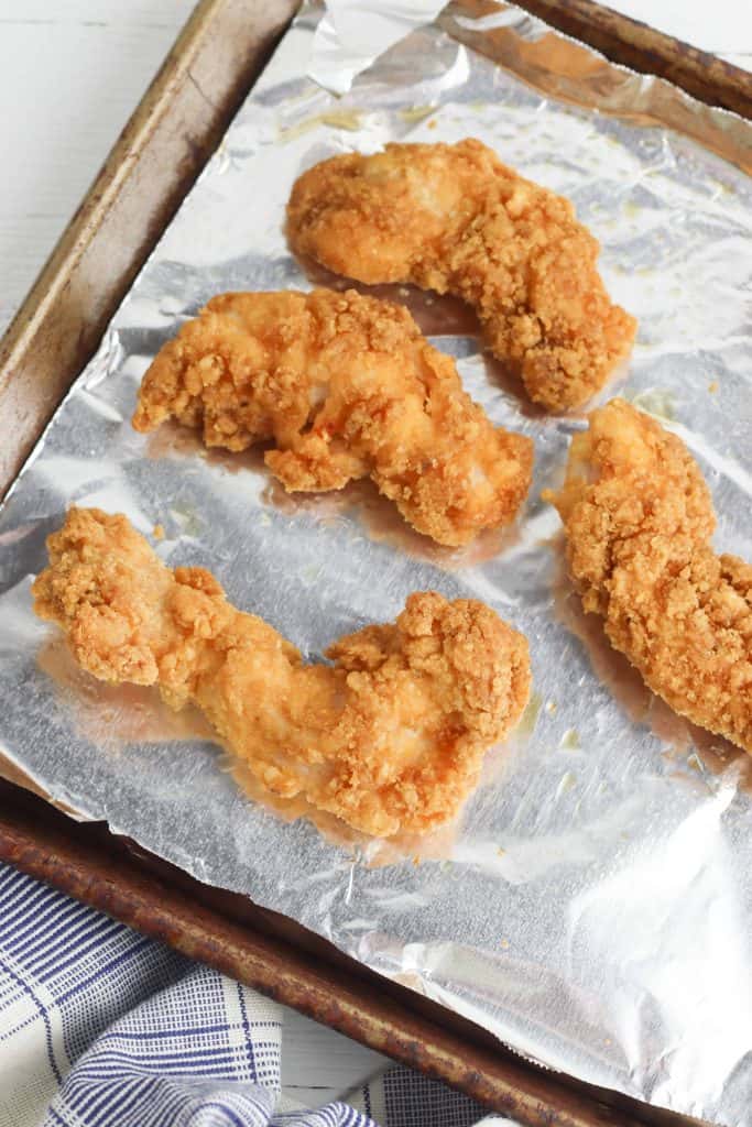 Chicken strips on foil lined baking sheet.