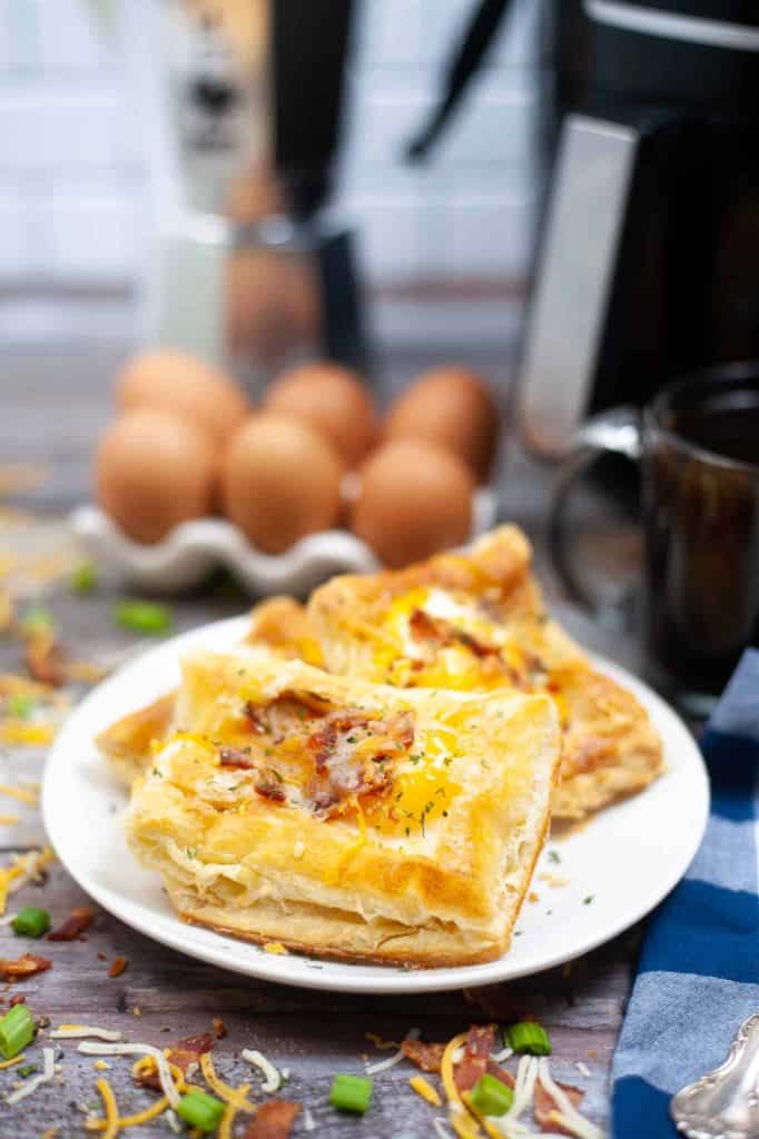 Bacon, egg and cheese pockets on a white plate in front of an air fryer.