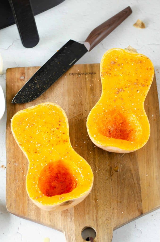 Butternut squash cut in half lengthwise with salt, pepper and cinnamon sprinkled on top.