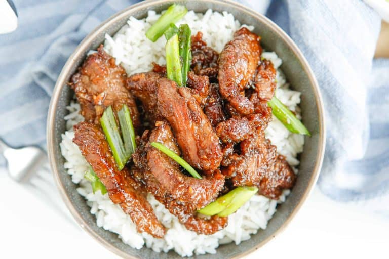 Overhead view of Mongolian beef over white rice in a bowl.