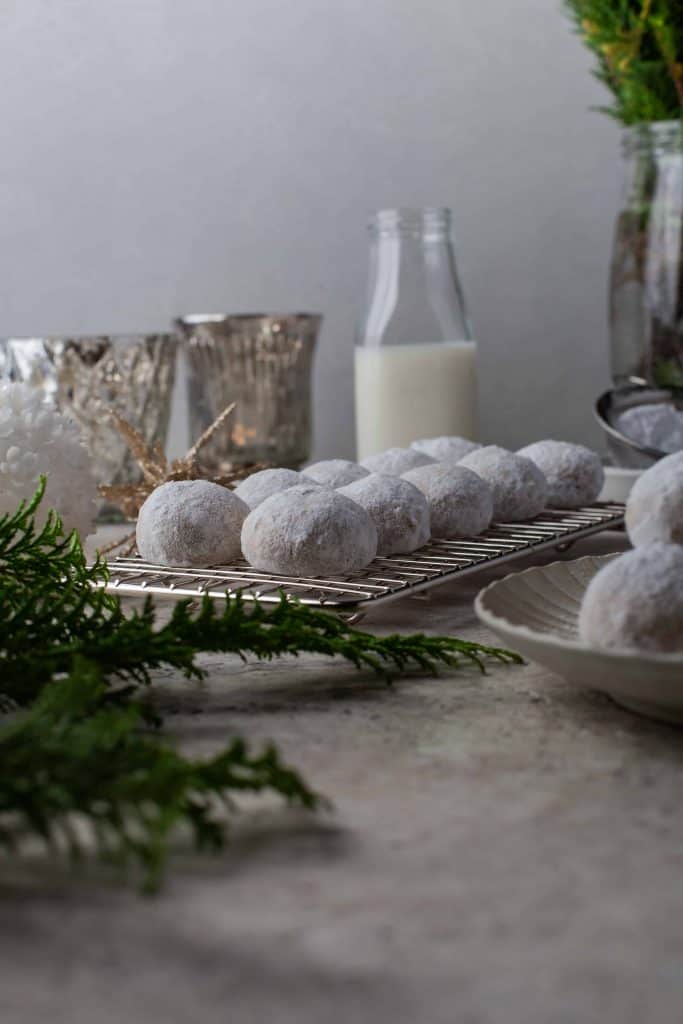 Snowball cookies on a cooling rack with milk and candles in the background.
