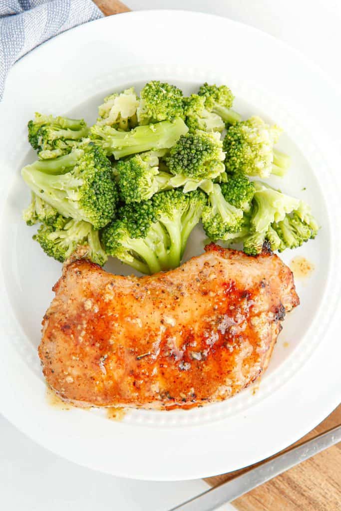 Overhead view of maple glazed pork chops with broccoli on a white plate.