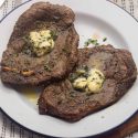 Air fryer steaks with herbed butter on a white plate.