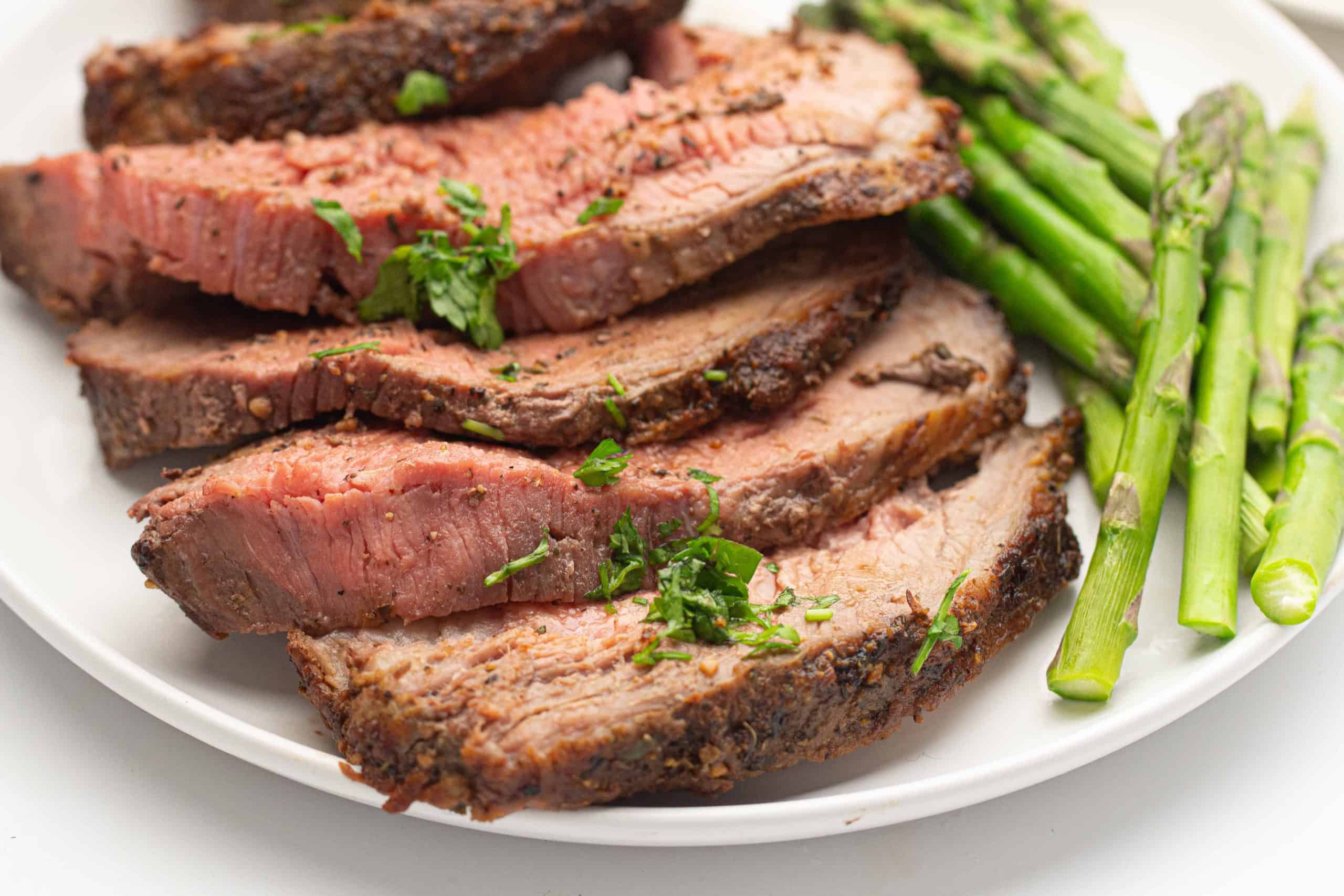 Sliced roast beef with a side of asparagus on a white plate.