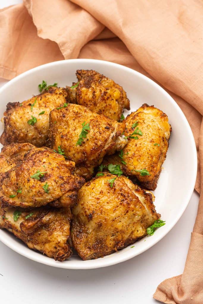 Cooked chicken thighs in a white bowl.