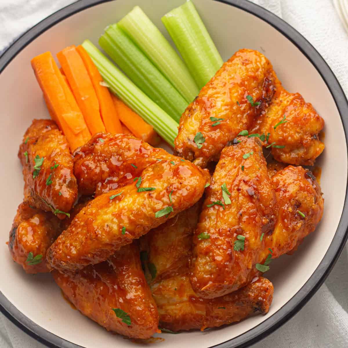 Overhead view of Air Fryer Buffalo Chicken wings on a white plate with celery and carrot sticks.