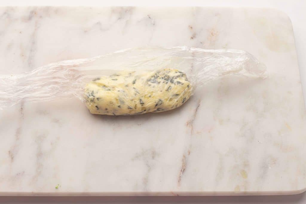 Roll of herbed butter in plastic wrap.