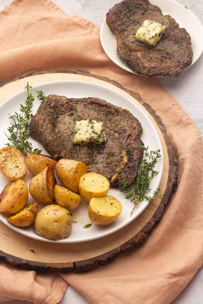 Steak and potatoes with herbs on a white plate.