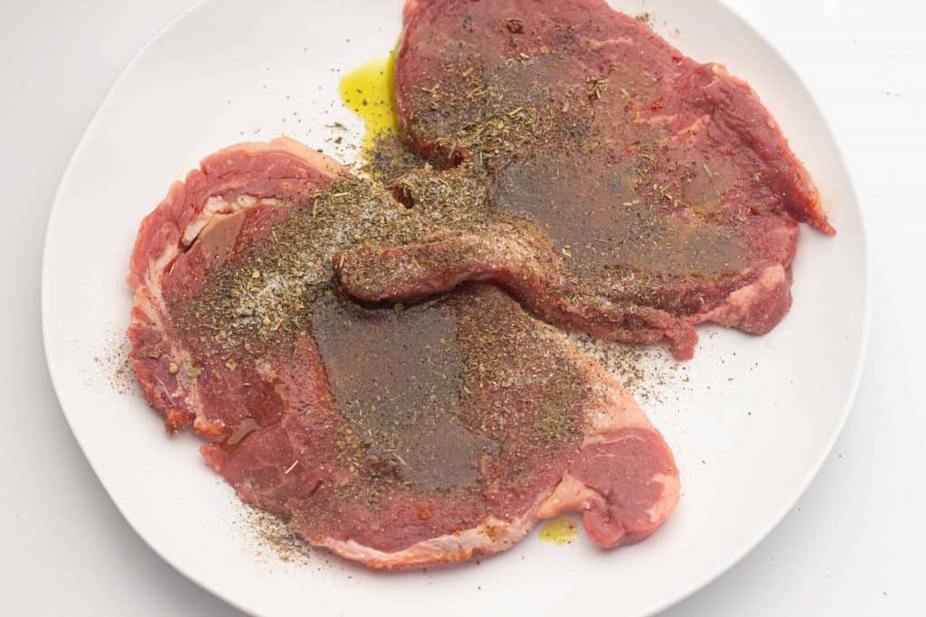 Steak on a white plate with herbs and oil.